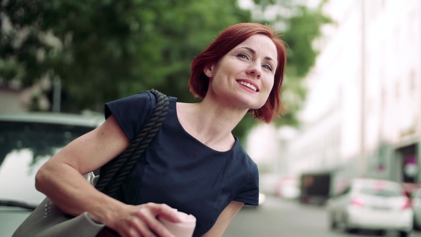 Young woman commuter with coffee standing outdoors in city, waiting for somebody. Slow motion.