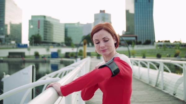 A young woman resting after doing exercise on bridge outdoors in city, using smartphone.