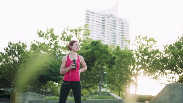 A young woman with earphones standing outdoors in city, resting after exercise.