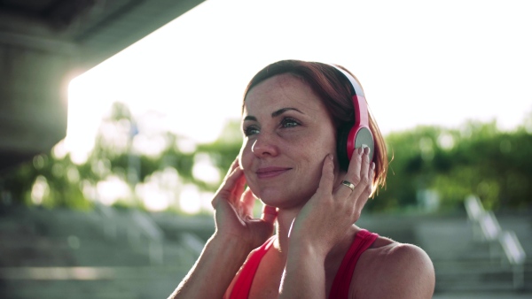 A young woman with headphones resting after doing exercise outdoors in city.