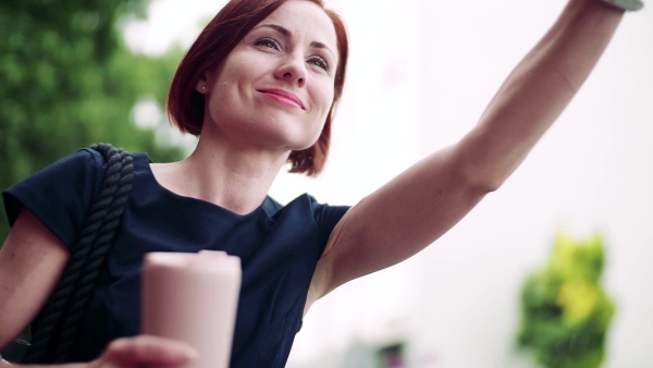 Young woman commuter with coffee standing outdoors in city, waving. Slow motion.