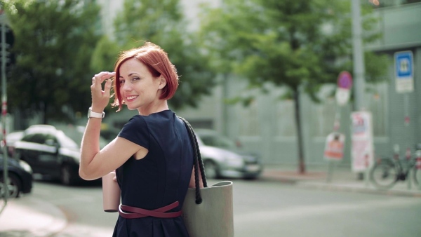 Young woman commuter with coffee walking outdoors in city. Slow motion.