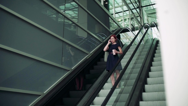 Young woman commuter with smartphone and coffee using escalator outdoors in city. Slow motion.