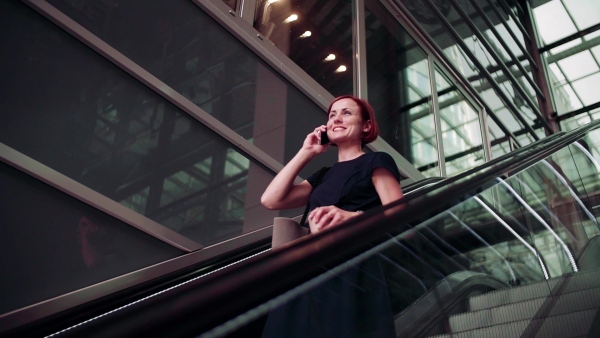 Young woman commuter with smartphone and coffee using escalator outdoors in city. Slow motion.