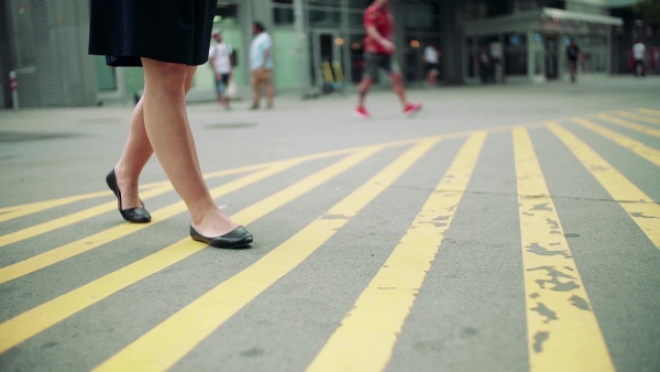 Midsection of young woman commuter walking outdoors in city on zebra crossing. Slow motion.