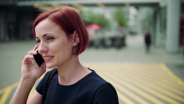 Young woman commuter with smartphone standing outdoors in city, making a call. Slow motion.