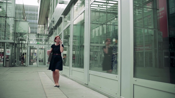 Young woman commuter with smartphone and coffee walking outdoors in city. Slow motion.