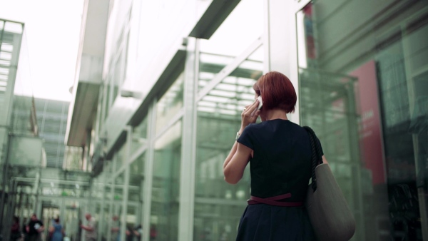 Young woman commuter with smartphone and coffee walking outdoors in city. Slow motion.