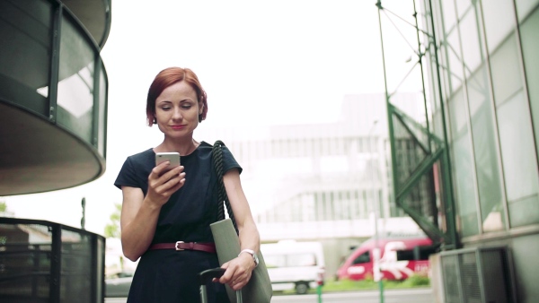 Young woman commuter with smartphone standing outdoors in city. Slow motion.