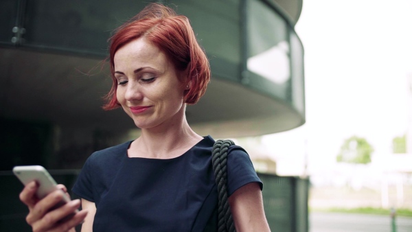 Young woman commuter with smartphone standing outdoors in city. Slow motion.