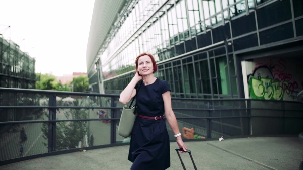 Young woman commuter with suitcase walking outdoors in city. Slow motion.