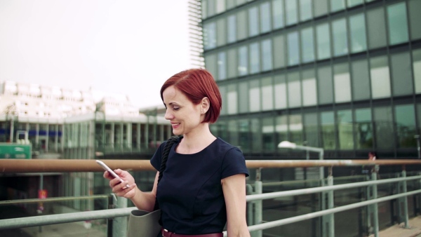 Young woman commuter with smartphone walking on bridge outdoors in city. Slow motion.