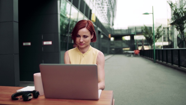 A young businesswoman with laptop sitting in cafe outdoors in city, working.