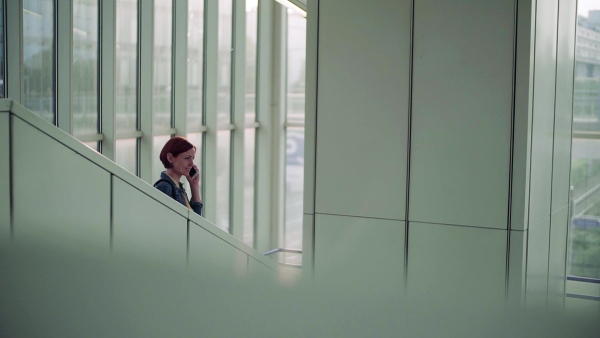 Young woman commuter with smartphone standing indoors in city, making a call. Slow motion.