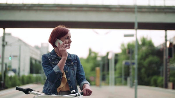 Young woman commuter with smartphone and bicycle standing outdoors in city. Slow motion.