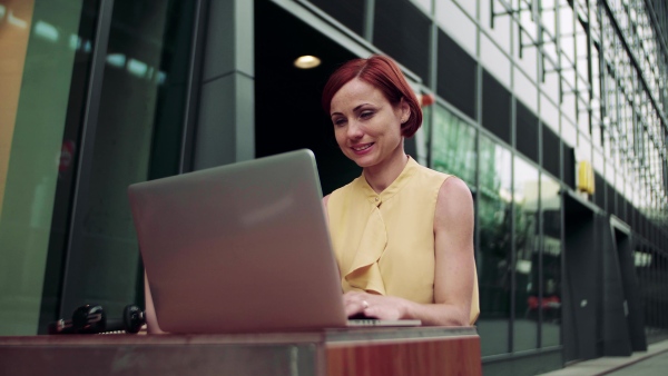 A young businesswoman with laptop sitting in cafe outdoors in city, working.