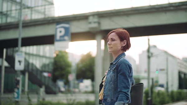 Young woman commuter standing outdoors on station in city, waiting for the train. Slow motion.