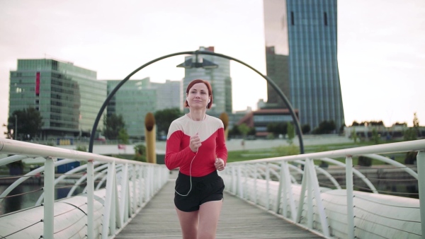 A young woman with earphones doing exercise on bridge outdoors in city, running. Slow motion.