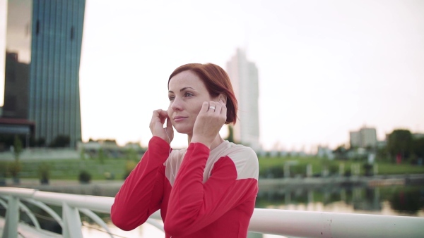 Young woman with earphones on bridge outdoors in city, resting after exercise. Slow motion.