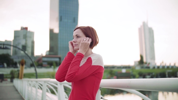 A young woman with earphones on bridge outdoors in city, resting after exercise. Slow motion.