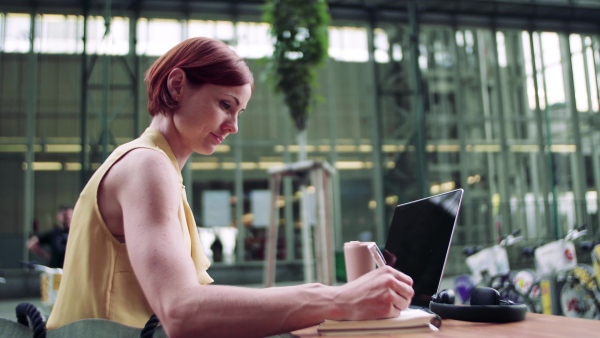 A young businesswoman with laptop sitting in cafe outdoors in city, working.