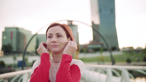 Young woman with earphones on bridge outdoors in city, resting after exercise. Slow motion.