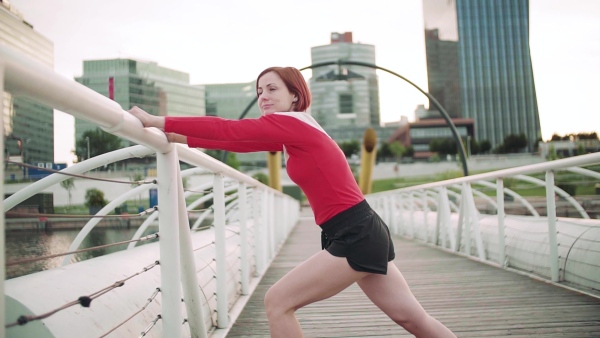 Young woman doing exercise on bridge outdoors in city, stretching. Slow motion.