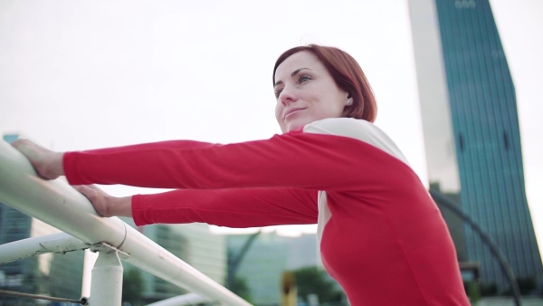 Young woman doing exercise on bridge outdoors in city, stretching. Slow motion.