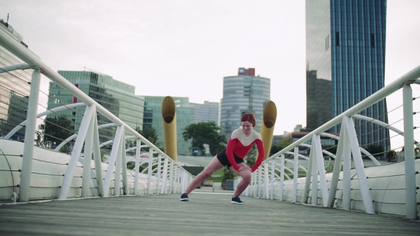 Young woman doing exercise on bridge outdoors in city, stretching. Slow motion.