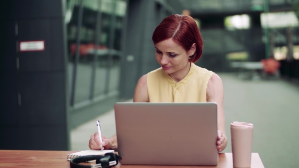 A young businesswoman with laptop sitting in cafe outdoors in city, working.