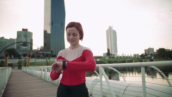 Young woman with smartwatch on bridge outdoors in city, resting after exercise. Slow motion.