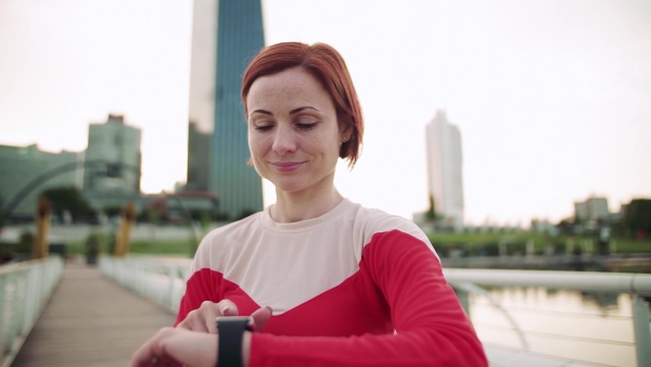 Young woman with smartwatch on bridge outdoors in city, resting after exercise. Slow motion.