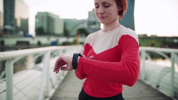 Young woman with smartwatch on bridge outdoors in city, resting after exercise. Slow motion.