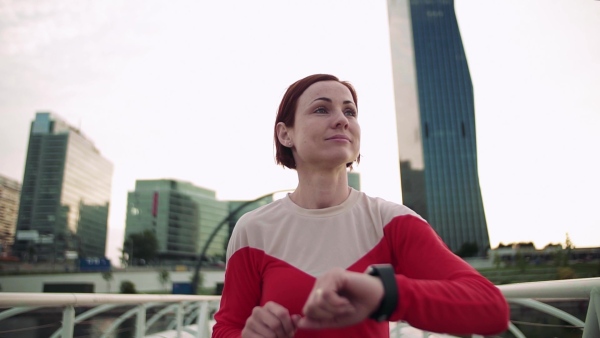 Young woman with smartwatch on bridge outdoors in city, resting after exercise. Slow motion.