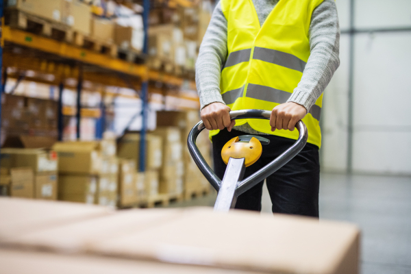 Unrecognizable male warehouse worker pulling a pallet truck with boxes.