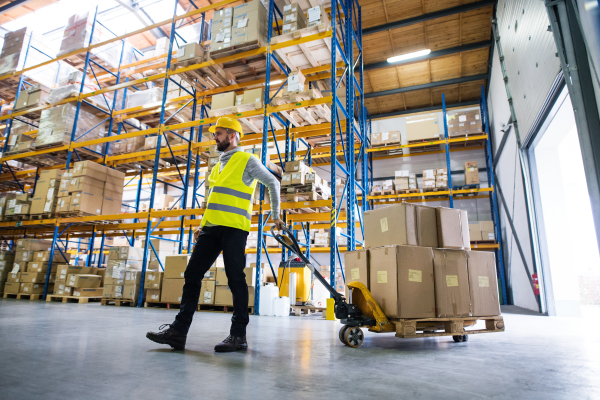 Young male warehouse worker pulling a pallet truck with boxes.