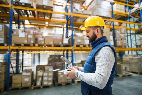 Man or a worker with tablet and drone controller standing in a warehouse.