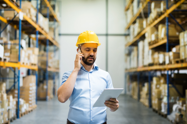 Warehouse worker or supervisor with a tablet and a smartphone, making a phone call.