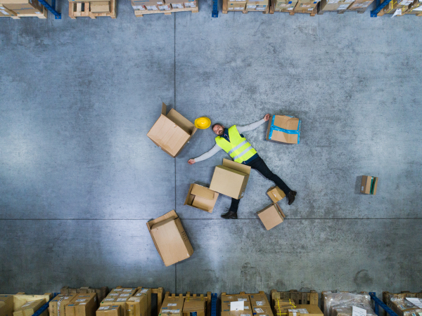 An accident in a warehouse. Man lying on the floor among boxes, unconscious. Aerial view.