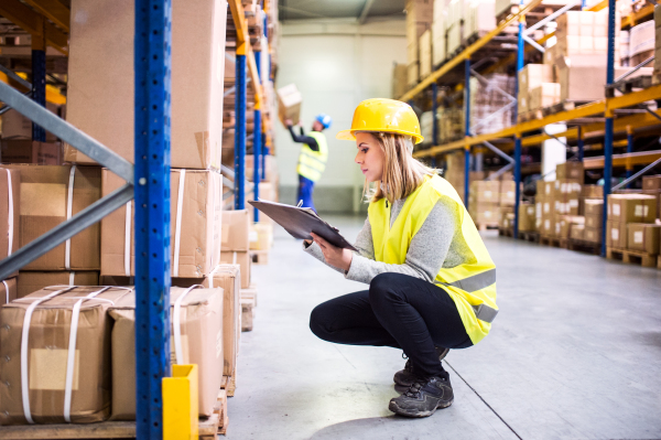 Young woman worker or supervisor with clipboard. Warehouse workers controlling stock.