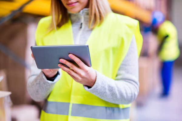 Unrecognizable young woman worker or supervisor with tablet. Warehouse workers controlling stock.