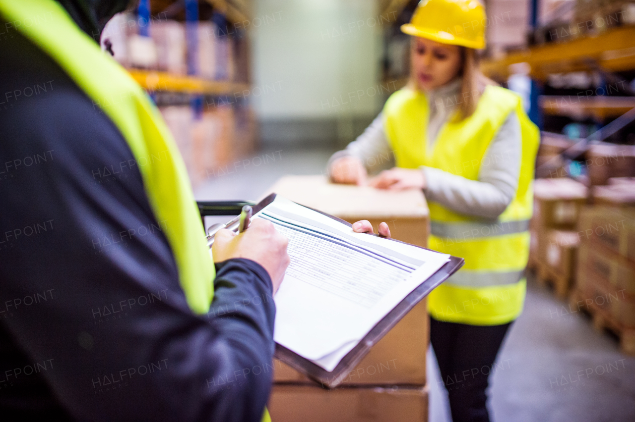 Young warehouse workers working together. Man and woman discussing something, making notes.