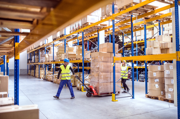 Young warehouse workers pulling a pallet truck with boxes.