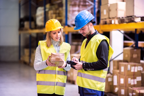 Young warehouse workers with barcode scanner working together. Man and woman discussing something.