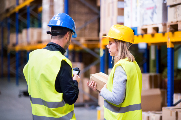 Young warehouse workers with barcode scanner working together. Man and woman discussing something.