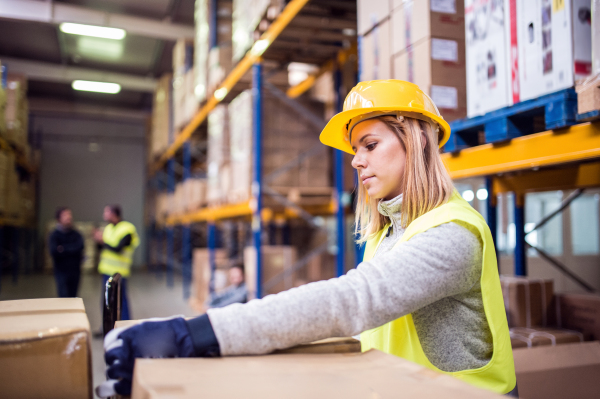 Young female warehouse worker loading up a pallet truck with boxes.