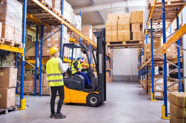 Young workers working together. Man forklift driver and a woman in a warehouse.