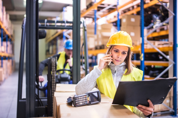 Young warehouse workers with smartphone and barcode scanner working together.