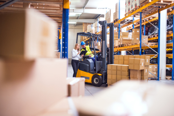 Young workers working together. Man forklift driver and a woman in a warehouse.