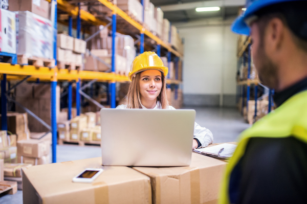 Young workers with laptop and smartphone, working together in a warehouse.